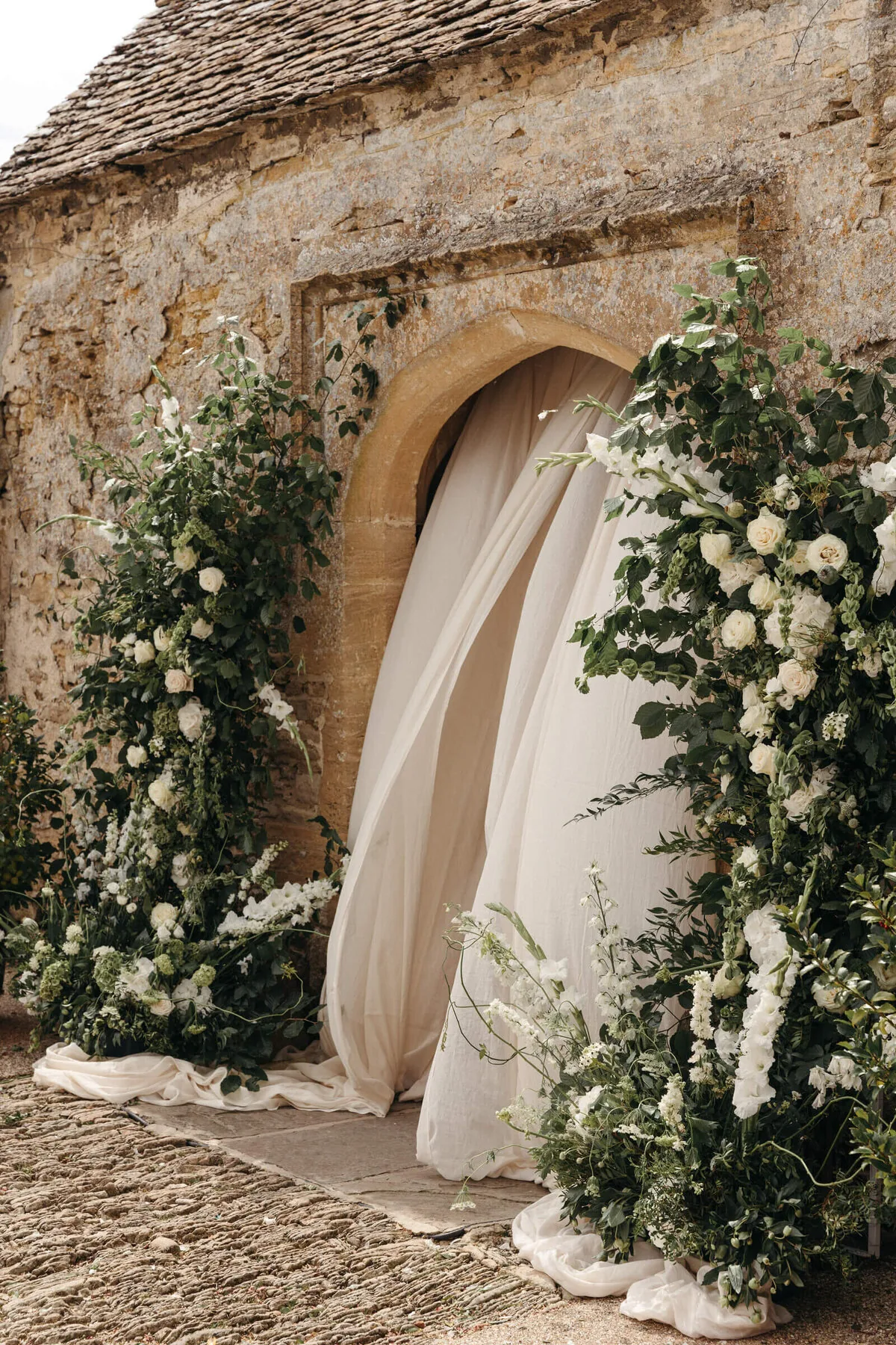 An outdoor wedding ceremony at Caswell House, with a white floral archway and draped fabric