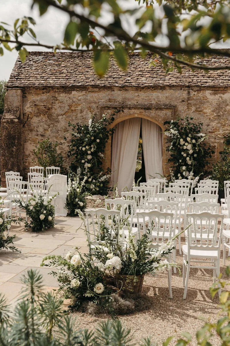 Outdoor ceremony with Cotswold stone and white floral arch